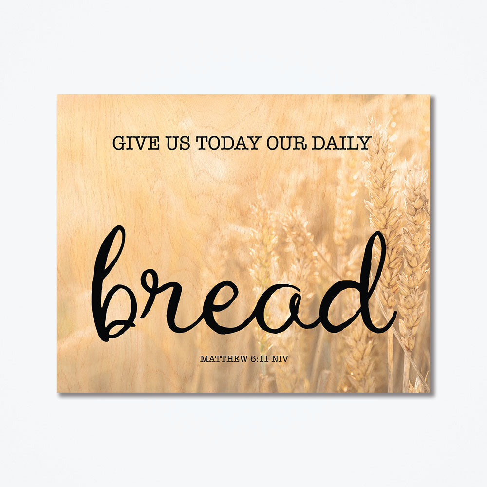 Wood poster with text that says, "give us today out daily bread" printed in black text with a wheat background.