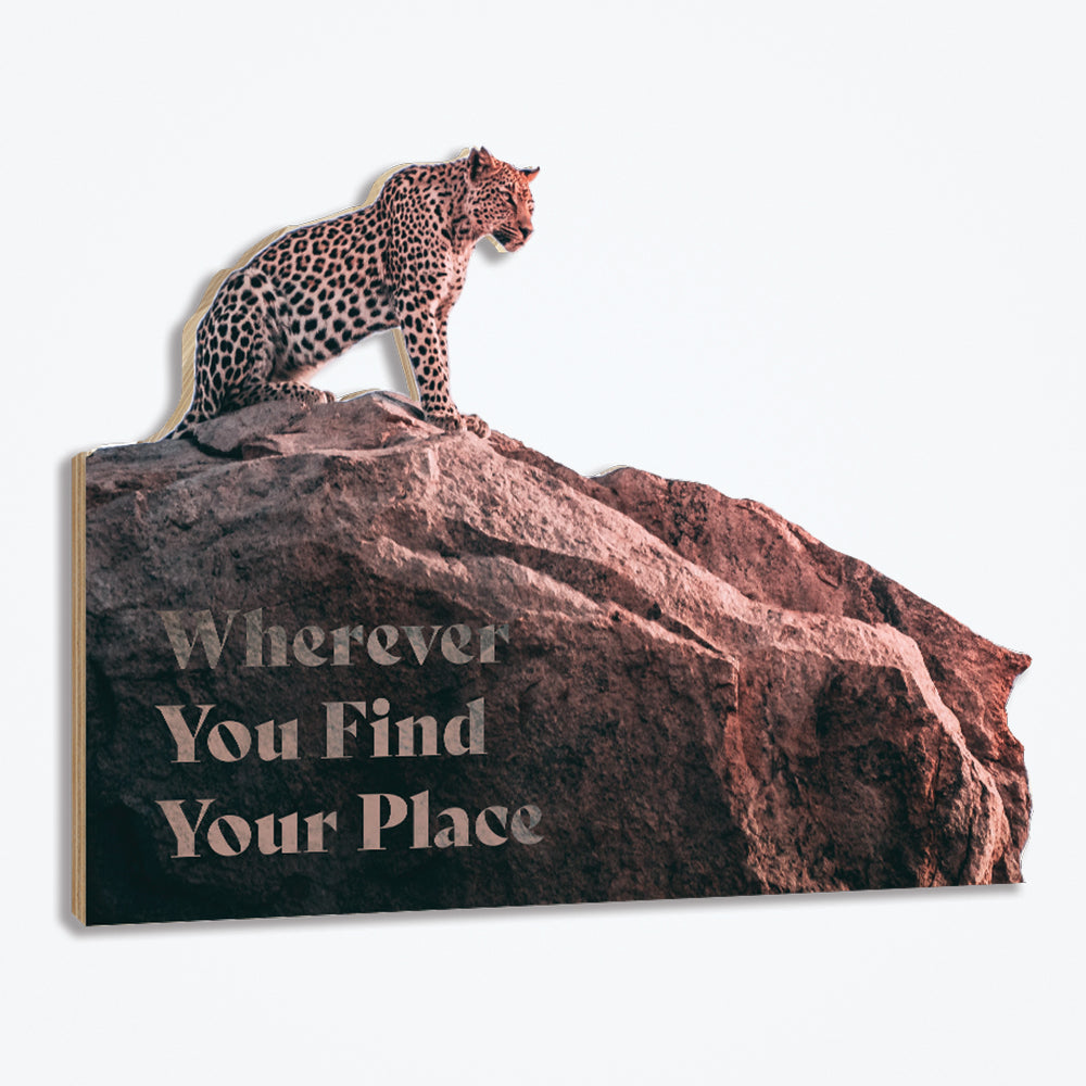 A cut to shape wood panel with a leopard sitting proudly on top of a mountain.